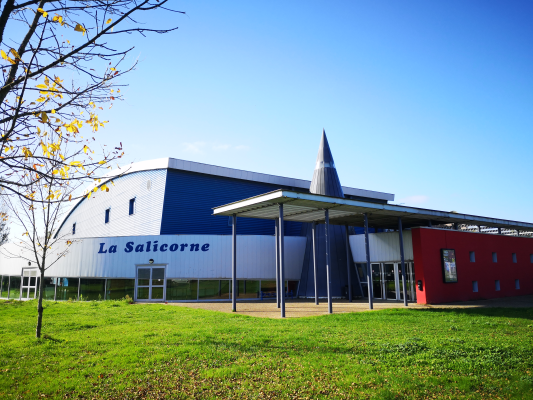 Un bâtiment industriel avec un panneau indiquant "La Salicorne", une pelouse verte et des arbres à feuilles caduques.
