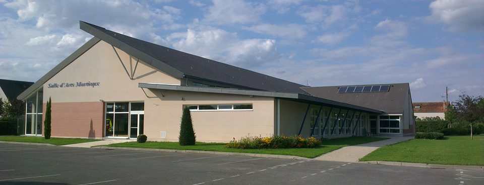 Bâtiment avec entrée, fenêtres, panneau "Salle d’Arts Martiniques", panneaux solaires, parking et végétation.