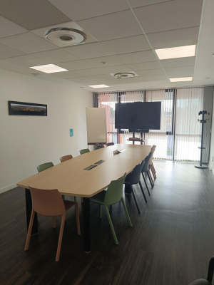 Salle avec table, chaises, écran et porte vitrée.