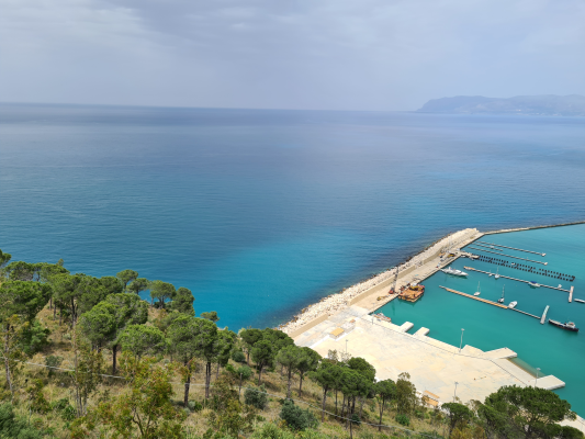 Vue sur mer avec plage, digue et port de plaisance.