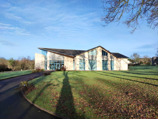 Bâtiment moderne avec grandes fenêtres, pelouse, arbre et ciel bleu.