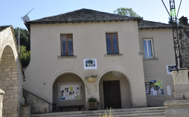 Bâtiment avec deux portes et deux fenêtres, affiches, plantes et antenne sur le toit.