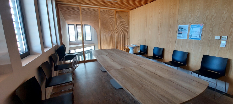 Salle de réunion avec grande table, chaises, tableau d'affichage et fenêtres.