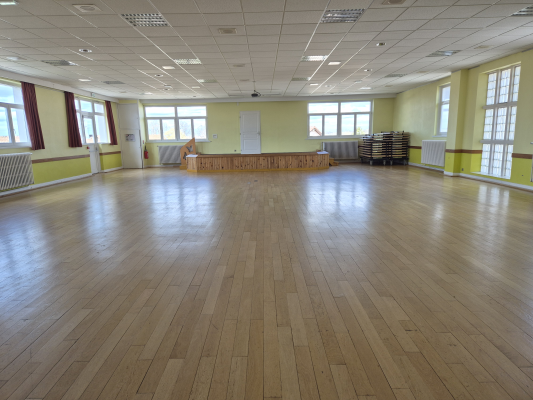 Salle spacieuse avec parquet, tables empilées, tableau blanc et grand miroir.
