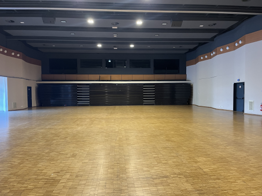 Salle spacieuse avec plancher en bois, rangées de chaises et murs blancs et bleus.