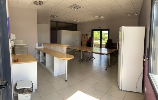 Salle avec tables, chaises, armoires, porte, fenêtre, frigo, évier, poubelle.