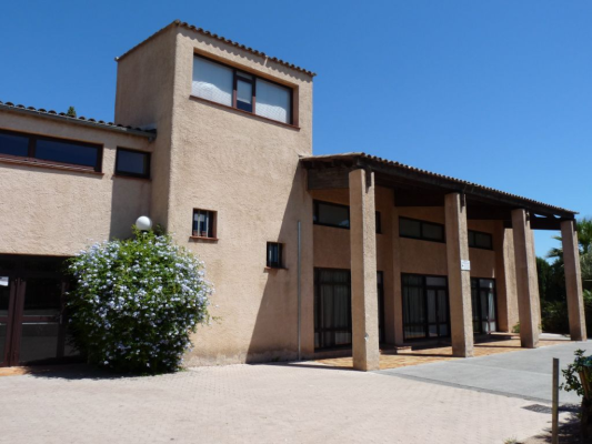Bâtiment moderne avec toits plats, colonnes et fenêtres. Arbre et réverbère devant.