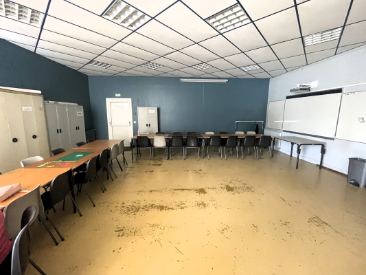 Salle avec tables, chaises, armoires, tableau blanc et projecteur.
