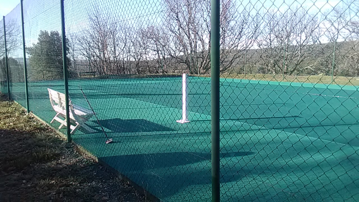 Terrain de tennis avec filet, chaises et clôture.