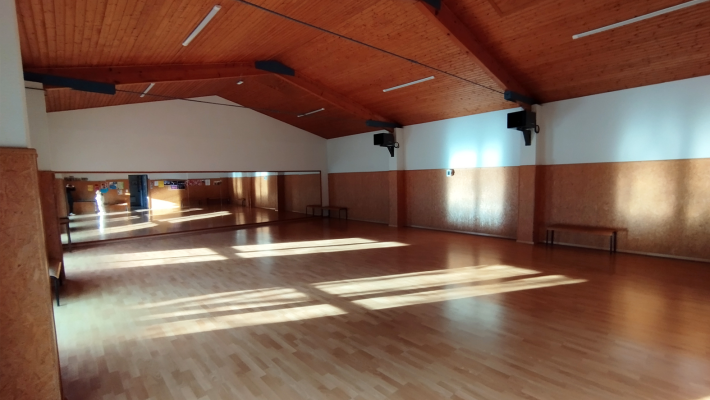 Salle avec plancher en bois, bancs, miroirs et plafonnier.