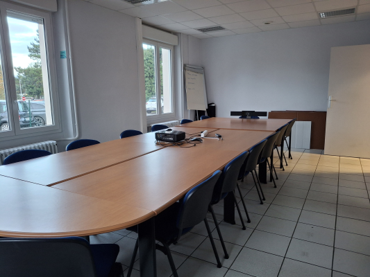 Salle de réunion avec table, chaises, projecteur et écran.
