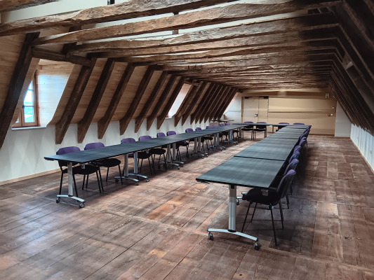 Salle avec tables, chaises et poutres apparentes.