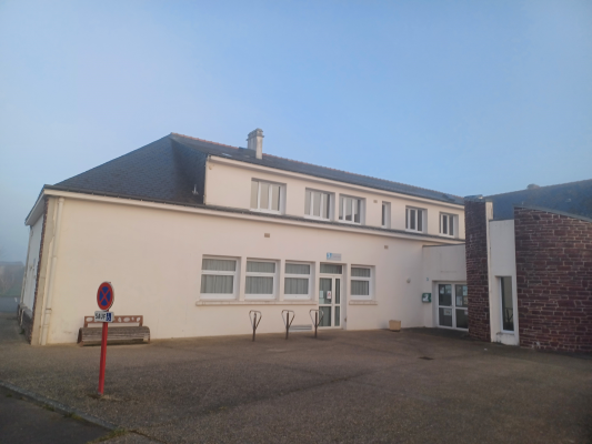 Bâtiment avec fenêtres, portes et stationnement. Panneau d'interdiction et banc visible.