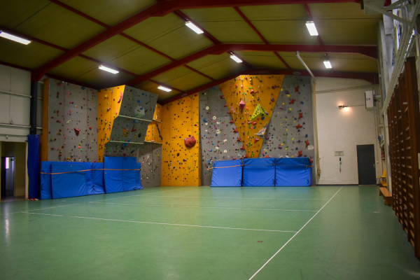 Salle d'escalade avec murs d'escalade, tapis de sécurité, sol vert et éclairage.