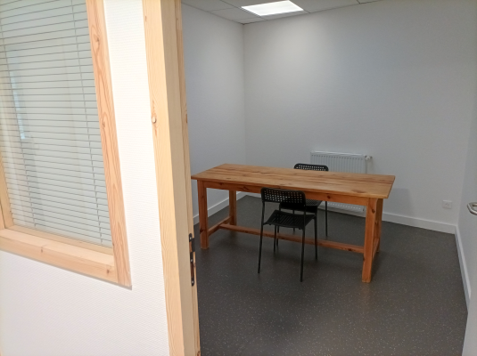 Pièce avec table en bois, deux chaises noires, radiateur et stores.
