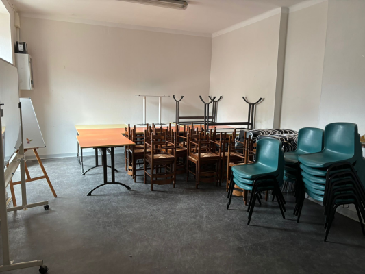 Salle avec tables, chaises, chevalet et tableau blanc.