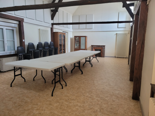 Salle avec tables, chaises, radiateurs, porte et fenêtres.