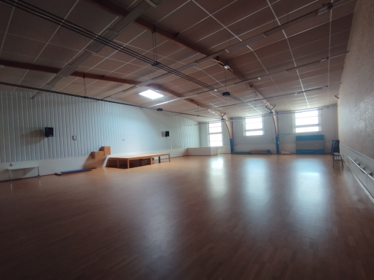 Salle spacieuse avec plancher en bois, banc, rampe de skate et fenêtres.