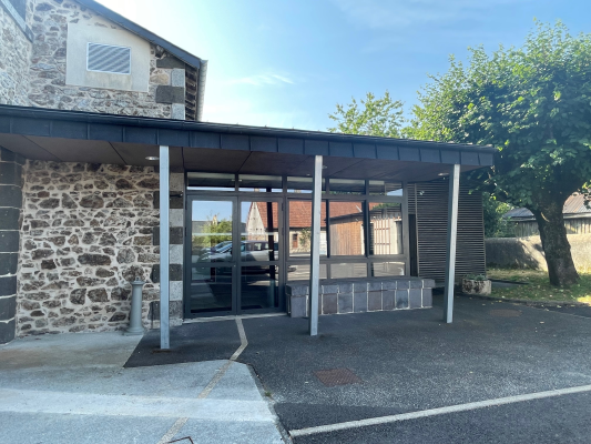 Station de taxi avec bâtiment en pierre, toit en métal, entrée en verre, voiture et arbres.