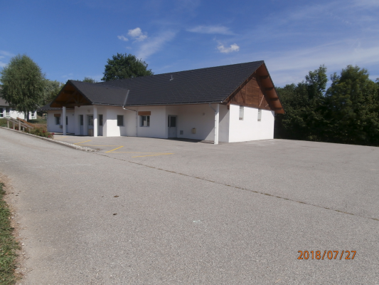 Un bâtiment blanc avec un toit en pente, une allée de gravier et des voitures garées.