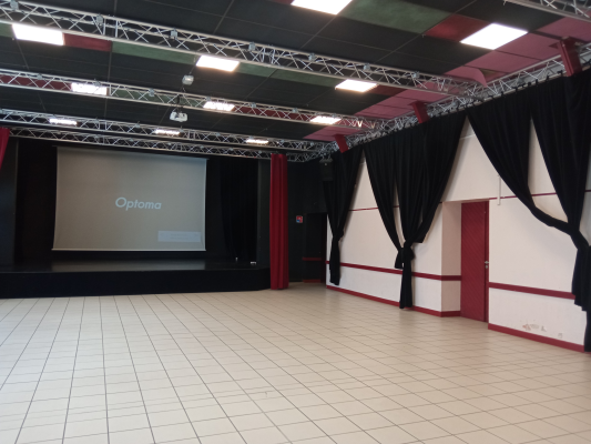 Salle avec écran, projecteur, structures métalliques, rideaux et sol carrelé.