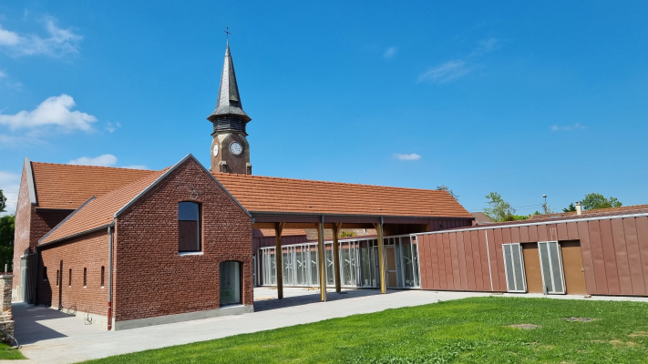 Église avec clocher, toit en tuiles, murs en briques, entrée vitrée et pelouse.