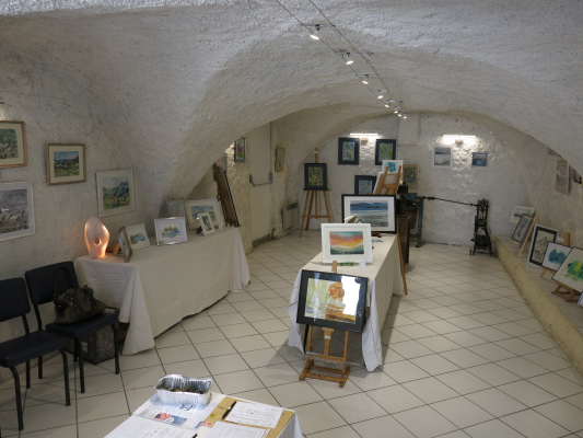 Salle voûtée avec tableaux, chevalets, tables et chaises.