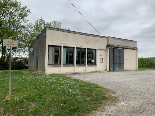 Bâtiment avec grandes fenêtres, porte de garage et panneau de signalisation à côté.