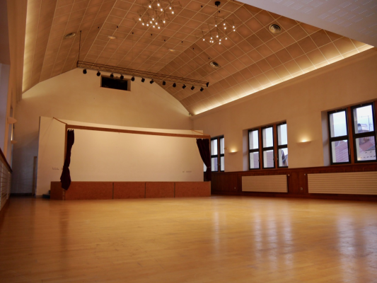 Salle avec plancher en bois, fenêtres, éclairage suspendu, écran, rideaux, et radiateurs.