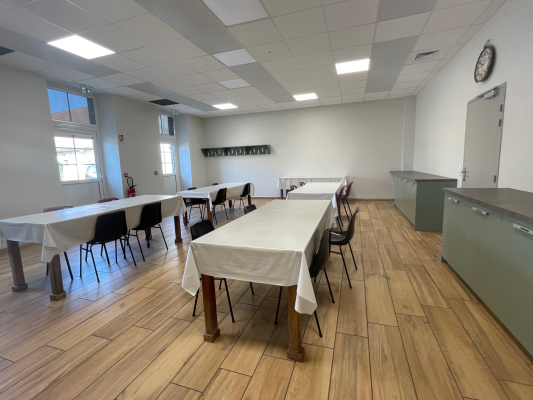 Salle avec tables, chaises, nappes, et meubles de rangement.