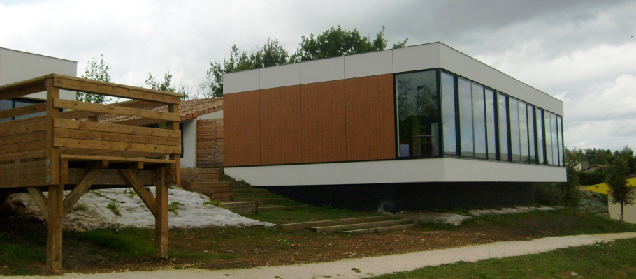 Maison moderne avec bois, verre, escalier en bois, terrain incliné, végétation.