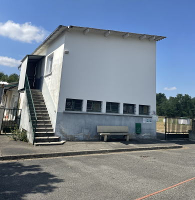 Bâtiment blanc avec escalier extérieur, banc et grillage.