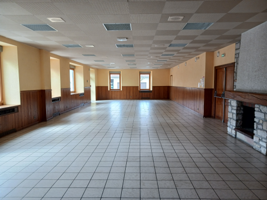 Salle spacieuse avec carrelage, boiseries, fenêtres, plaques chauffantes, cheminée et plafonnier.