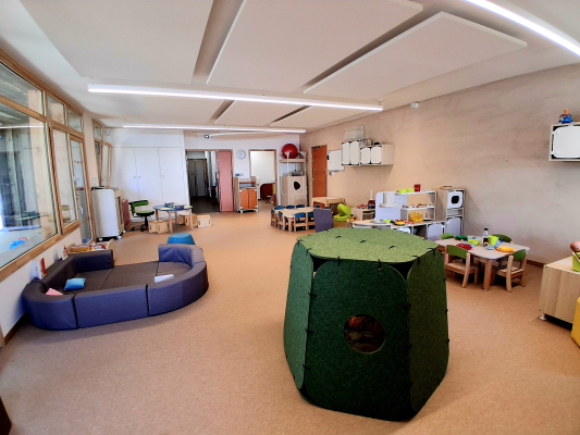 Salle avec canapés, tables, chaises, tentes et jouets.