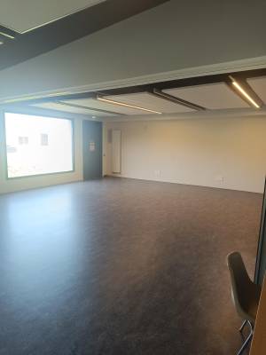 Salle vide avec sol, murs, fenêtres, portes et éclairage au plafond. Une chaise visible.