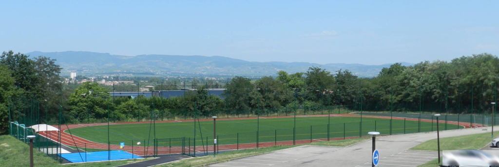 Stade de football avec piste d'athlétisme, parking et vue sur les montagnes.