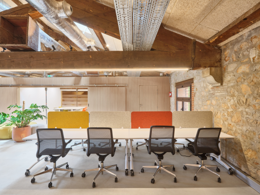 Salle de réunion avec table, chaises, murs en brique, ventilation apparente et plantes.