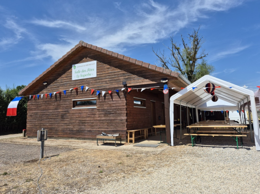 Bâtiment en bois avec enseigne, guirlandes, tables et bancs sous un auvent.