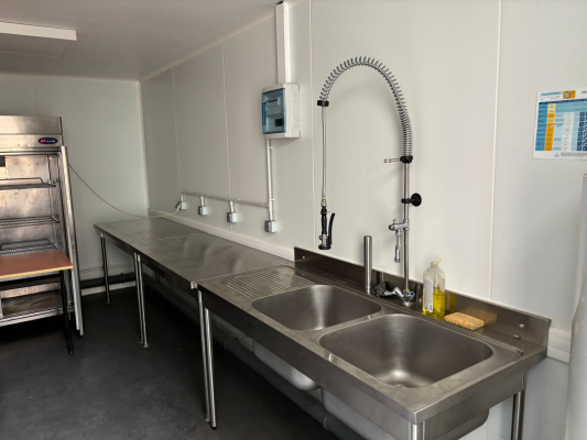 Cuisine avec plans de travail, évier, robinets, lave-mains, four et distributeur de savon.