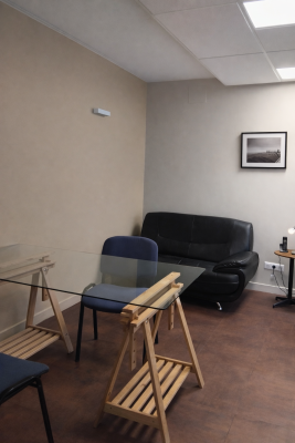 Salle avec canapé, table en verre, chaises pliantes et table de travail.