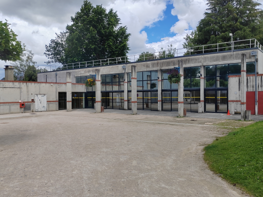 Bâtiment industriel avec grandes portes, fenêtres et parking en gravier.
