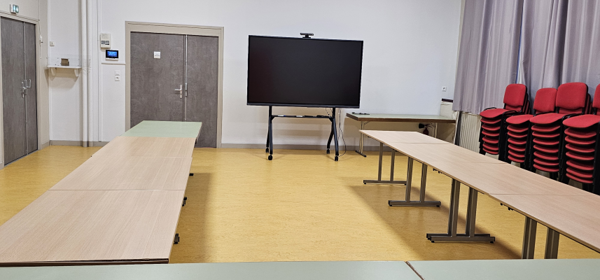 Salle avec écran, tables, chaises, vidéoprojecteur.