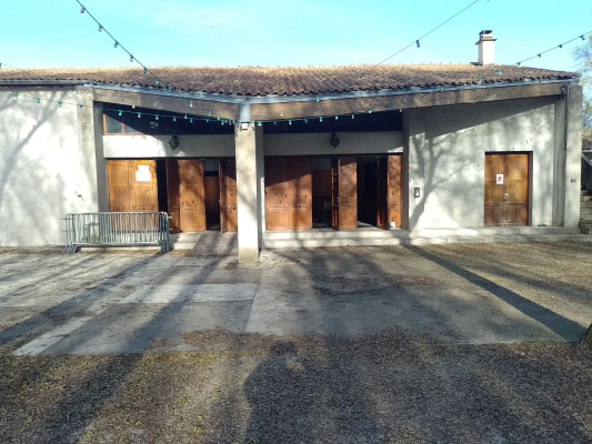 Bâtiment avec portes en bois, toit en tuiles, sol en gravier, rampes, et guirlandes lumineuses.