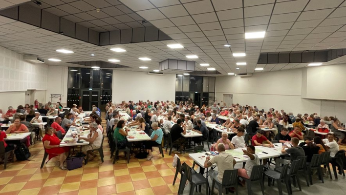 Salle de cantine avec tables, chaises, et personnes mangeant.