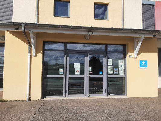 Entrée de bâtiment avec portes vitrées, auvent et panneaux d'affichage.