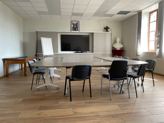 Salle avec table, chaises, tableau blanc, télévision et bureau.