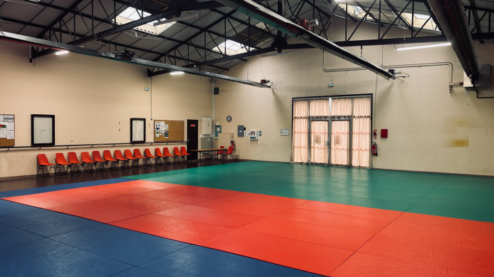 Salle avec tapis de combat, chaises, table et portes.