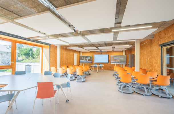 Salle de classe avec tables, chaises, tableau blanc et projecteur.