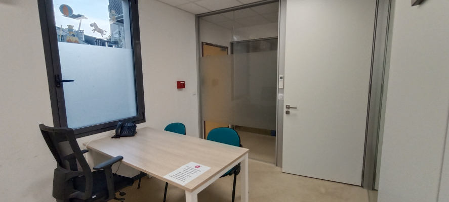 Salle avec table, chaises, téléphone, porte vitrée et porte blanche.