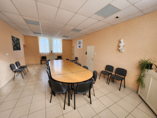 Salle de réunion avec table ovale, chaises, porte, fenêtre et plante.